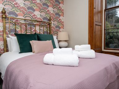 A bedroom with a brass bed frame pink quilted bedspread folded white towels on the bed patterned wallpaper and a window with wooden trim at Watermouth Castle Bassett Apartment Berrynarbor near Ilfracombe