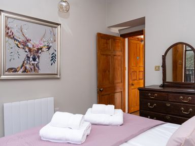 A bedroom with a bed with folded towels a wooden dresser with a mirror wooden doors and a painting of a deer at Watermouth Castle Bassett Apartment in Berrynarbor near Ilfracombe