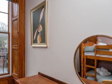 A wooden bunk bed reflected in a round mirror with a framed picture of a rabbit on the wall near a wooden window at Watermouth Castle Bassett Apartment Berrynarbor near Ilfracombe