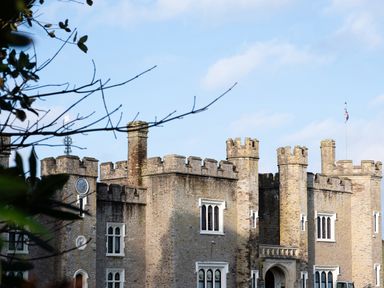 A stone castle with battlements chimneys and arched windows under a blue sky at Watermouth Castle Rhododendron Apartment Berrynarbor near Ilfracombe