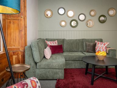 A living room with a green couch and round mirrors on the wall at Watermouth Castle Rhododendron Apartment Berrynarbor near Ilfracombe