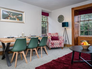 A dining area with green chairs and wooden table next to a patterned armchair and windows at Watermouth Castle Rhododendron Apartment Berrynarbor near Ilfracombe