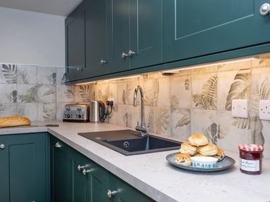 A kitchen countertop with a sink a toaster a kettle plates with scones and a jar of jam at Watermouth Castle Rhododendron Apartment Berrynarbor near Ilfracombe