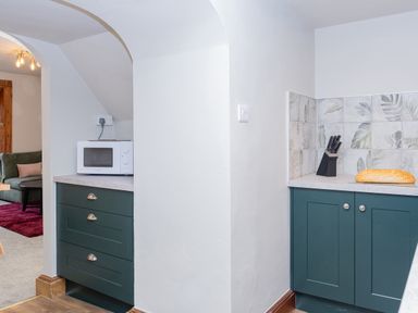 A kitchen corner with green cabinets a microwave a knife block and a loaf of bread at Watermouth Castle Rhododendron Apartment Berrynarbor near Ilfracombe
