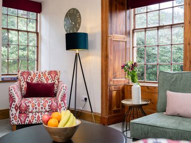A sitting area with patterned armchair green sofa fruit bowl and flowers at Watermouth Castle Rhododendron Apartment Berrynarbor near Ilfracombe