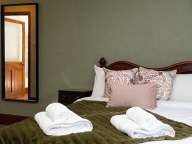 A bed with pillows and folded towels with a mirror reflecting a wooden door in a bedroom at Watermouth Castle Rhododendron Apartment Berrynarbor near Ilfracombe