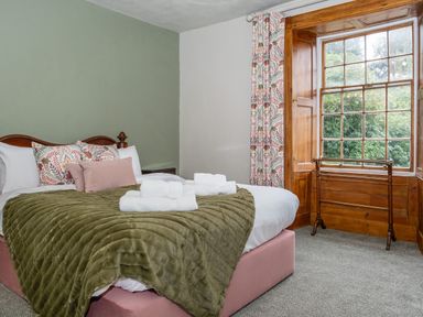 A bedroom with a bed with pillows and towels near a window with wooden trim at Watermouth Castle Rhododendron Apartment Berrynarbor near Ilfracombe