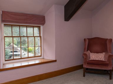 A corner of a room with a pink upholstered armchair and a wooden framed window with a wooden sill at Watermouth Castle Rhododendron Apartment Berrynarbor near Ilfracombe
