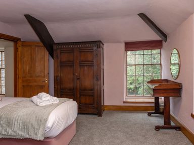 A bedroom with a bed and folded towels an antique wardrobe a wooden desk with a mirror and a window showing greenery at Watermouth Castle Rhododendron Apartment Berrynarbor near Ilfracombe