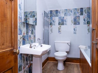 A bathroom with a sink toilet and bathtub with floral tiles on the walls at Watermouth Castle Rhododendron Apartment Berrynarbor near Ilfracombe