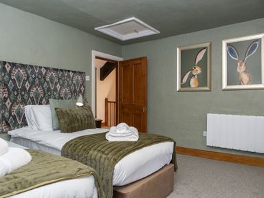 A bedroom with two single beds with green bedding and cushions a wooden door and framed rabbit pictures on the wall at Watermouth Castle Rhododendron Apartment Berrynarbor near Ilfracombe