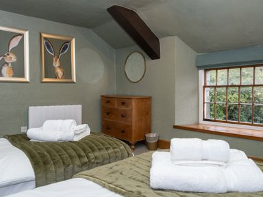 A bedroom with two beds with white towels and green blankets a wooden chest of drawers a window and two framed pictures of rabbits on the wall at Watermouth Castle Rhododendron Apartment in Berrynarbor near Ilfracombe