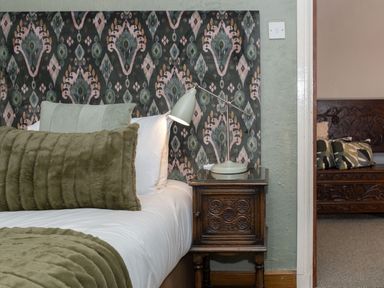 A bed with green cushions and a bedside table with a lamp next to a doorway showing a wooden bench with cushions at Watermouth Castle Rhododendron Apartment Berrynarbor near Ilfracombe