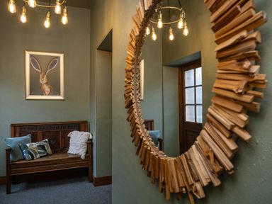 A hallway with a wooden bench with cushions a framed picture of a rabbit a round wooden-framed mirror and a wooden door at Watermouth Castle Rhododendron Apartment Berrynarbor near Ilfracombe