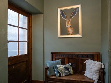 A wooden bench with three cushions below a wall painting of a hare next to a wooden door at Watermouth Castle Rhododendron Apartment Berrynarbor near Ilfracombe
