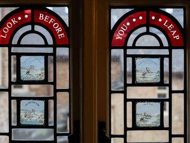 A stained glass window with red panels saying look before you leap and illustrated bird images at Watermouth Castle Rhododendron Apartment Berrynarbor near Ilfracombe