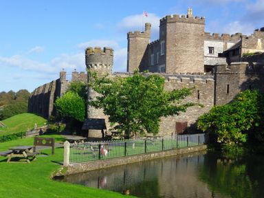 A stone castle with towers and battlements near a grassy area and a pond at Watermouth Castle Rhododendron Apartment Berrynarbor near Ilfracombe