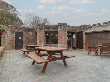 An outdoor seating area with tables and benches at Watermouth Castle, Rhododendron Apartment in Berrynarbor near Ilfracombe