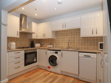 A kitchen with white cabinets a washing machine a dishwasher an oven and a kettle at Ger Y Lli in Rhosneigr
