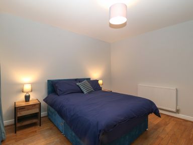 A bedroom with a double bed with blue bedding two bedside tables with lamps and wooden floor at Ger Y Lli in Rhosneigr