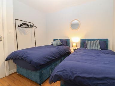 A bedroom with two single beds with blue bedding a lamp in between and a clothing rack with hangers at Ger Y Lli in Rhosneigr
