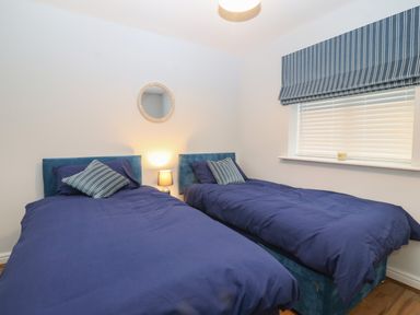 A bedroom with two single beds covered in blue bedding a striped window blind a round wall mirror and a small lamp on a bedside table at Ger Y Lli in Rhosneigr