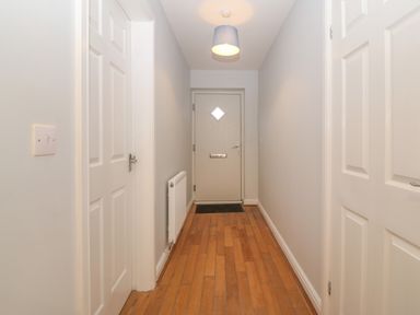 A hallway with wooden floor radiator light switch and three doors at Ger Y Lli in Rhosneigr