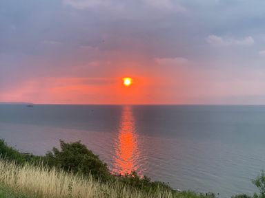 A sunset over the sea with reflected light on the water and grassy hillside in the foreground at The Artist's Cabin By The Sea in Herne Bay