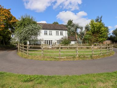 A white two-story house with multiple windows surrounded by trees and a wooden fence at Culver Court Cottage in Venny Tedburn near Crediton