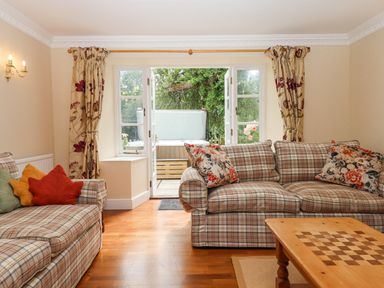 A living room with two plaid sofas and floral cushions with an open door showing a hot tub outside at Culver Court Cottage Venny Tedburn near Crediton