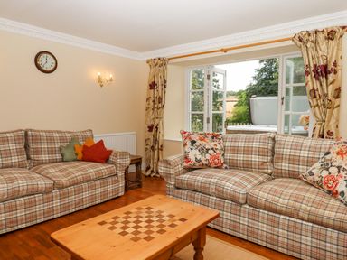 A living room with two plaid sofas a wooden coffee table and open windows showing a garden at Culver Court Cottage Venny Tedburn near Crediton