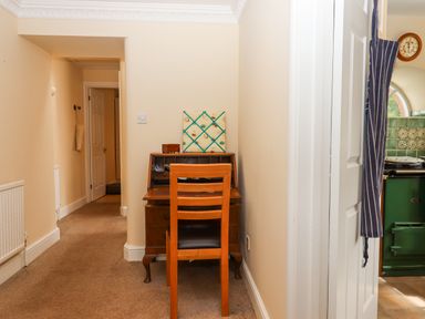 A hallway with a wooden desk and chair and a striped apron hanging near a kitchen at Culver Court Cottage Venny Tedburn near Crediton
