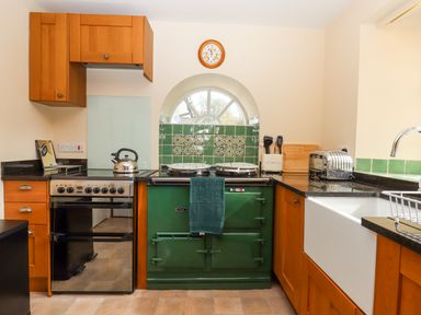 A kitchen with wooden cabinets a black oven a green Aga stove a white sink and a toaster at Culver Court Cottage Venny Tedburn near Crediton