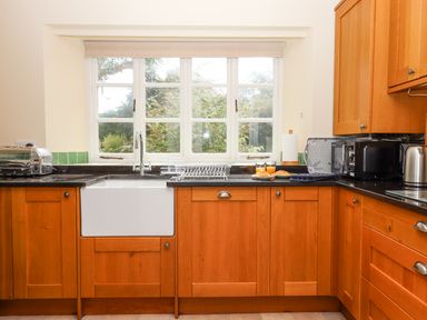A kitchen with wooden cabinets a white farmhouse sink and window at Culver Court Cottage in Venny Tedburn near Crediton
