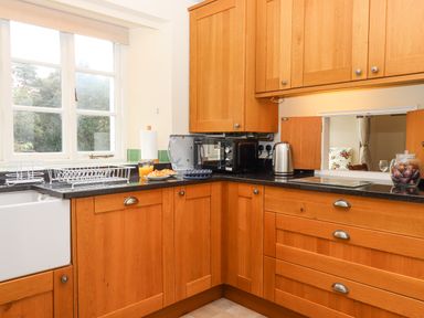 A kitchen with wooden cabinets a black countertop a microwave a kettle a glass of orange juice and a plate with croissants at Culver Court Cottage in Venny Tedburn near Crediton