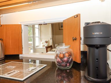 A kitchen countertop with a jar of coffee pods a Nespresso coffee machine and a pass-through window to a dining area at Culver Court Cottage Venny Tedburn near Crediton