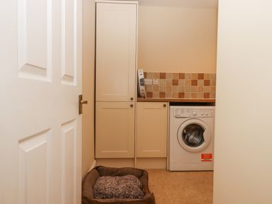 A laundry room with a washing machine, cabinets, a wooden countertop, tiled backsplash, and a pet bed at Culver Court Cottage in Venny Tedburn near Crediton