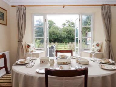 A dining room with a set table and open doors leading to a garden at Culver Court Cottage in Venny Tedburn near Crediton
