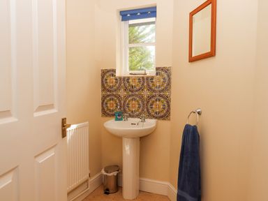 A small bathroom with a pedestal sink under a window with decorative tiles and a blue towel hanging on a ring Culver Court Cottage Venny Tedburn near Crediton