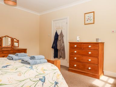 A bedroom with a wooden dresser a wooden chest of drawers a bed with folded towels and robes on a door at Culver Court Cottage in Venny Tedburn near Crediton