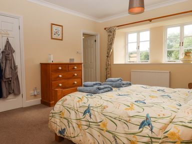 A bedroom with a bed with bird patterned bedding and folded towels on top a wooden chest of drawers and a window with floral curtains at Culver Court Cottage in Venny Tedburn near Crediton