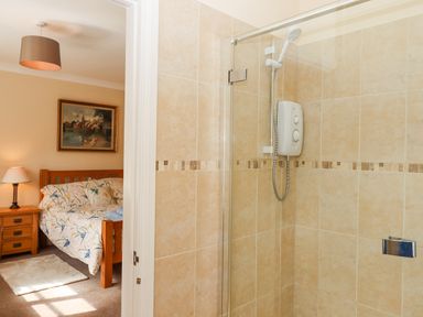 A tiled bathroom with a shower next to a bedroom with a wooden bed and bedside table at Culver Court Cottage in Venny Tedburn near Crediton