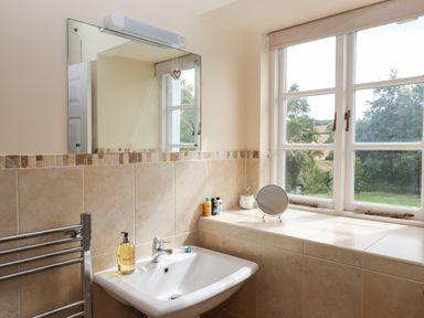 A bathroom with a sink mirror a towel rack and a window with a small round mirror on the windowsill at Culver Court Cottage in Venny Tedburn near Crediton