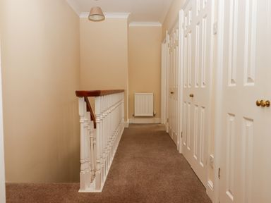 A hallway with beige walls carpet and multiple white doors and a white banister at Culver Court Cottage in Venny Tedburn near Crediton