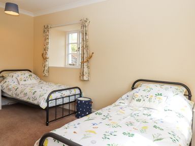 A bedroom with two single metal frame beds with floral bedding and a window with floral curtains at Culver Court Cottage in Venny Tedburn near Crediton