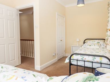 A bedroom with two single beds a nightstand with a lamp a closet and an open door showing a hallway at Culver Court Cottage in Venny Tedburn near Crediton
