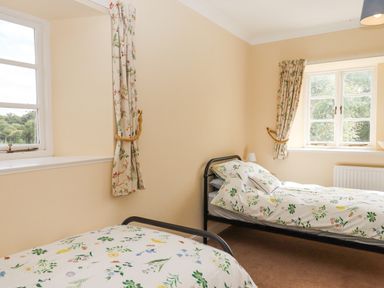 A bedroom with two single beds with floral bedding and windows with curtains at Culver Court Cottage in Venny Tedburn near Crediton
