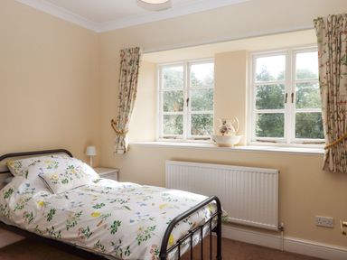 A bedroom with a single bed beside a window with curtains and a pitcher on the windowsill at Culver Court Cottage in Venny Tedburn near Crediton