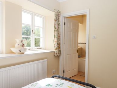 A bedroom window with a ceramic pitcher and bowl on the sill and an open door leading to a bathroom at Culver Court Cottage in Venny Tedburn near Crediton