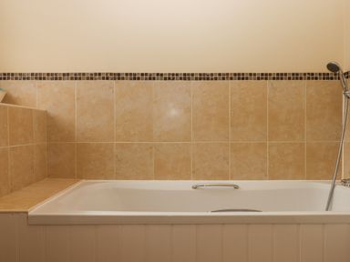 A bathroom with a bathtub surrounded by beige tiles and a handheld shower at Culver Court Cottage in Venny Tedburn near Crediton